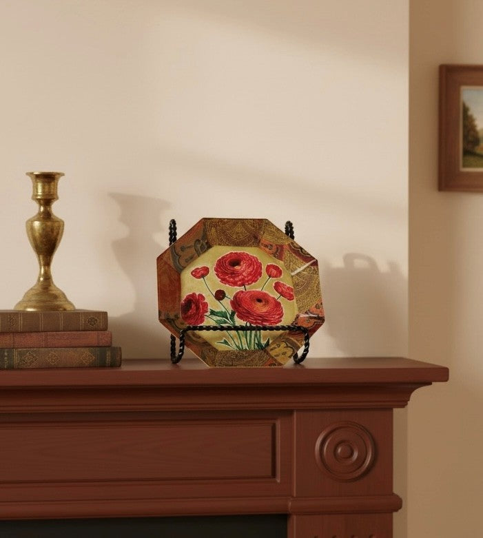 Decorative plate with ranunculus flowers on a stand on a mantle with a candle holder and books.