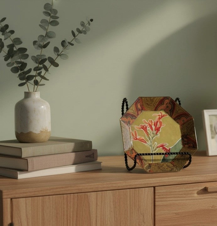 Decorative plate with a large freesia in the middle on a credenza with other items.