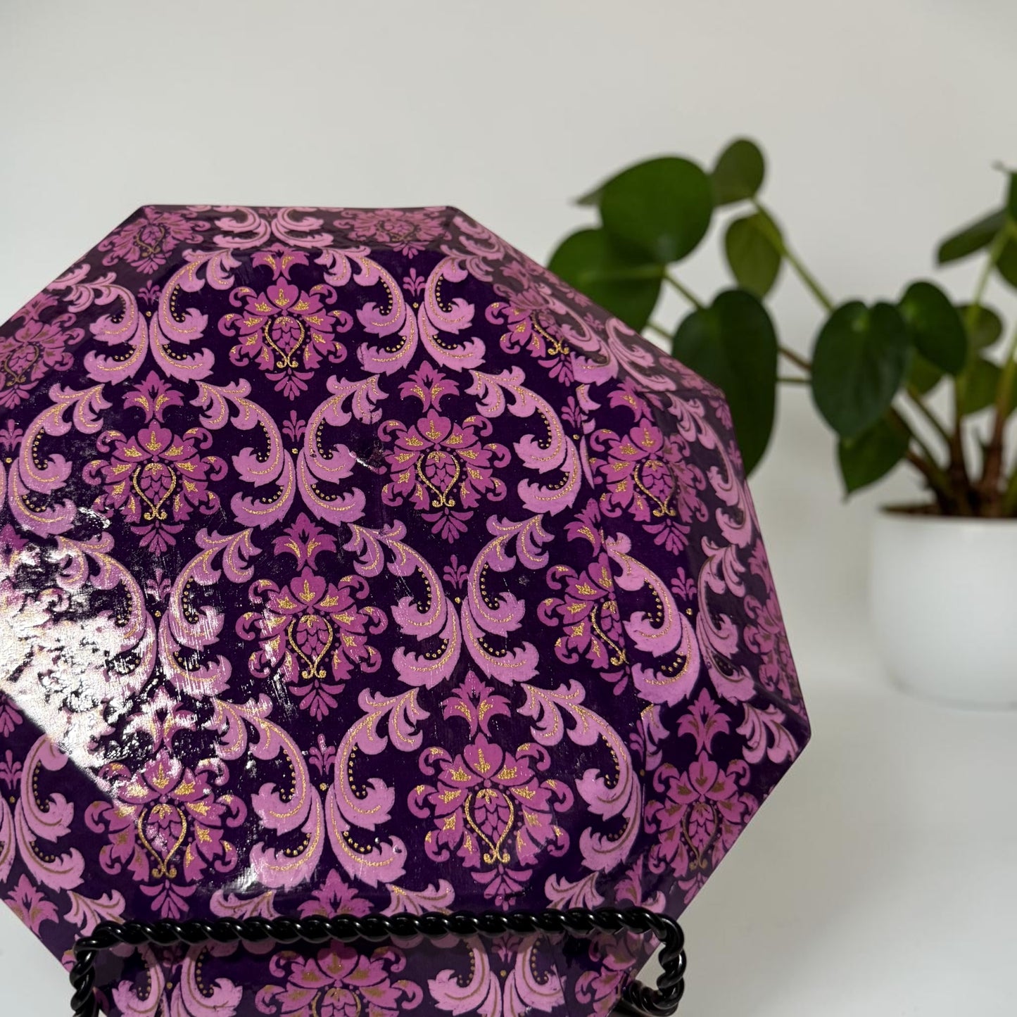 Backside of a large octagonal plate with a purple patterned design on a white surface with a plant in the background