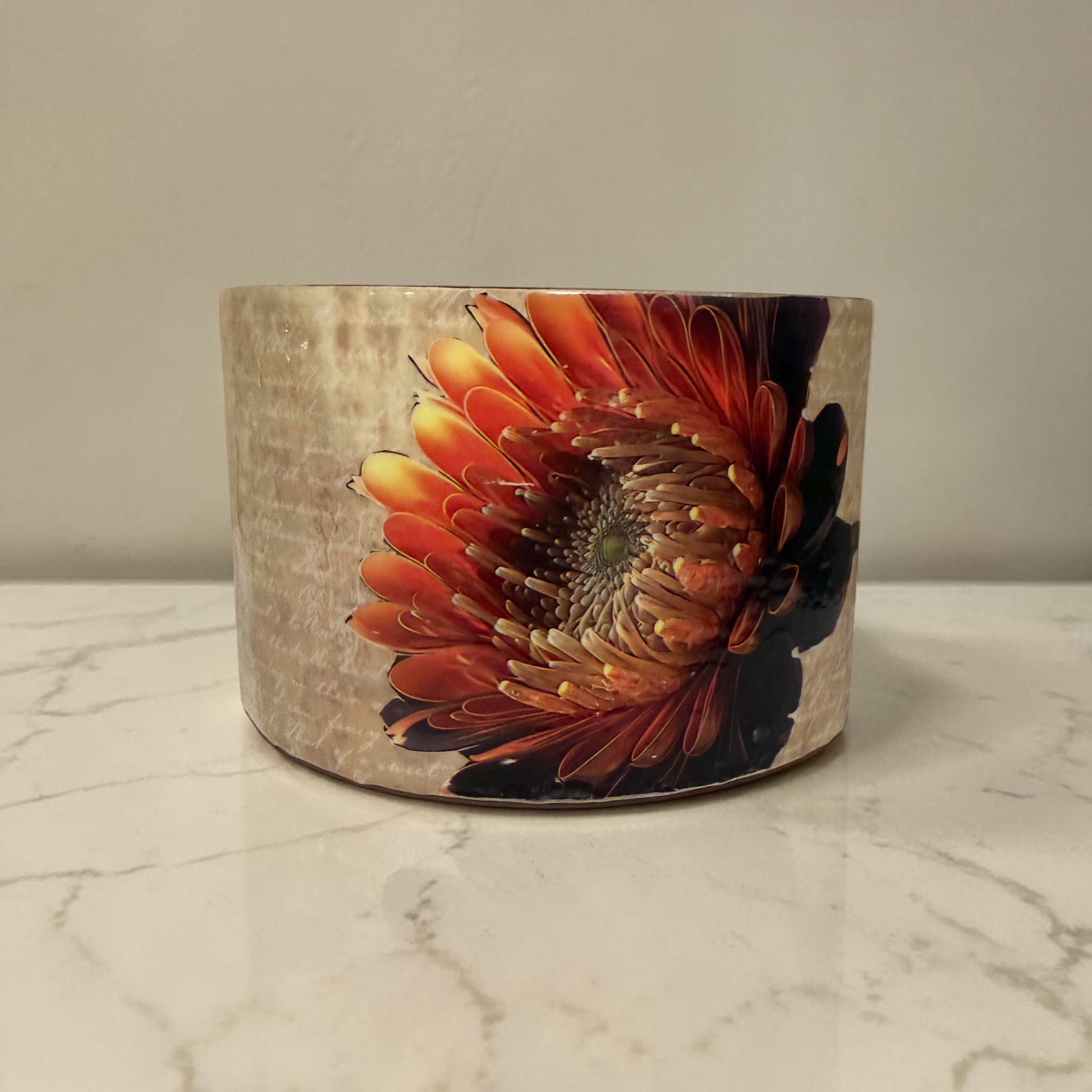 Oval glass vase decorated with beige paper with white writing in the background and a large brilliant flower. 
