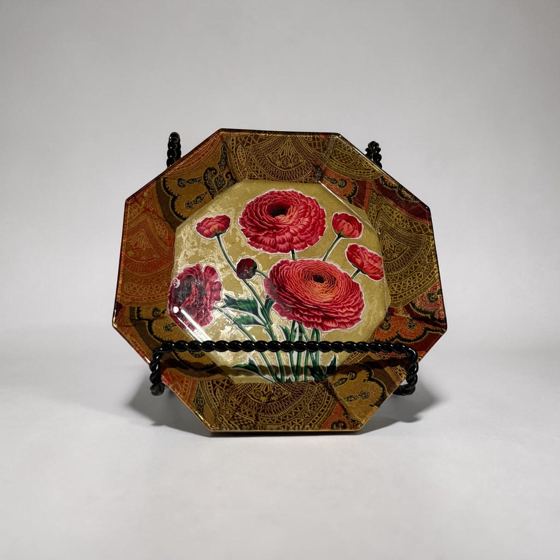 Octagonal plate decorated with ranunculus flowers on a stand against a white background