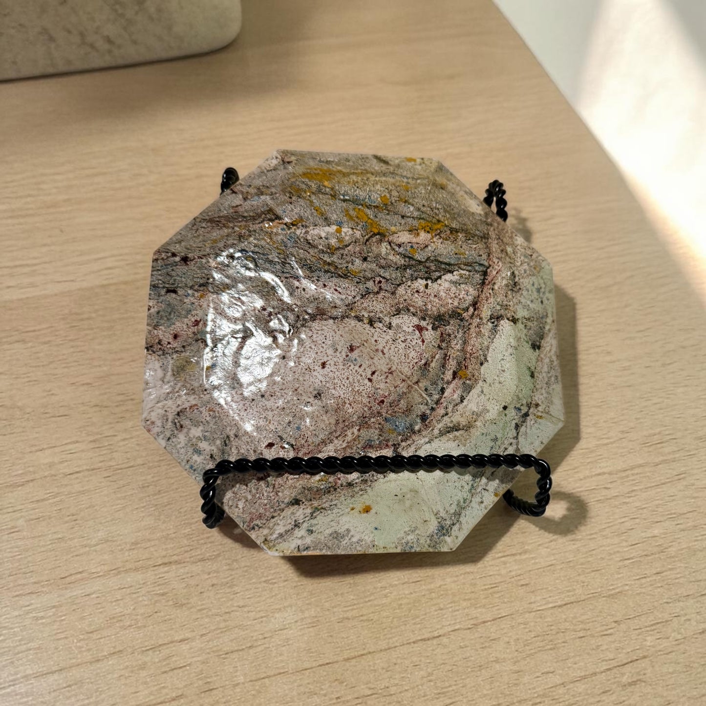 The back of a decorative plate with a marbled design on a stand on a light wood surface.