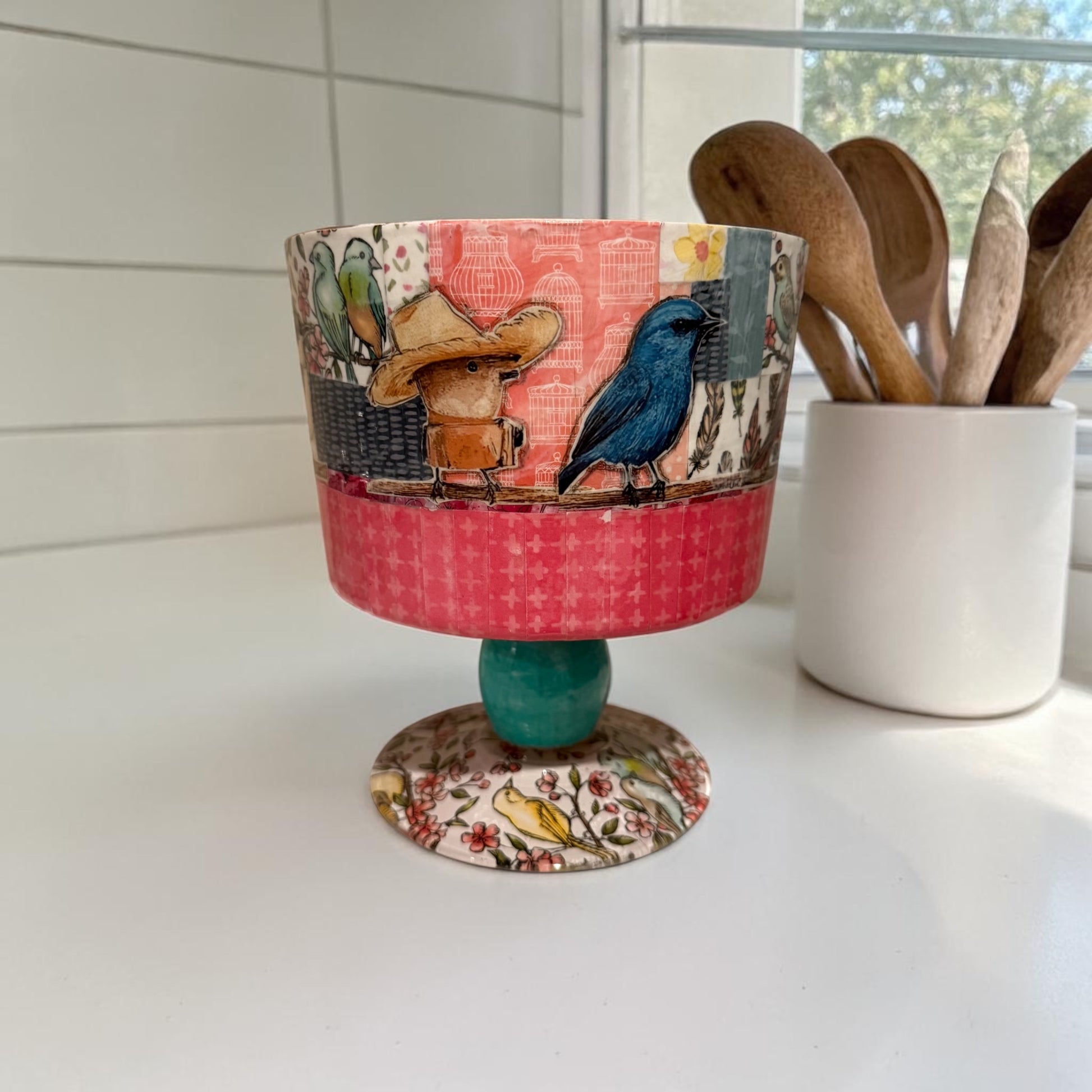 Decorative trifle bowl on a kitchen counter next to a jar of kitchen spoons.