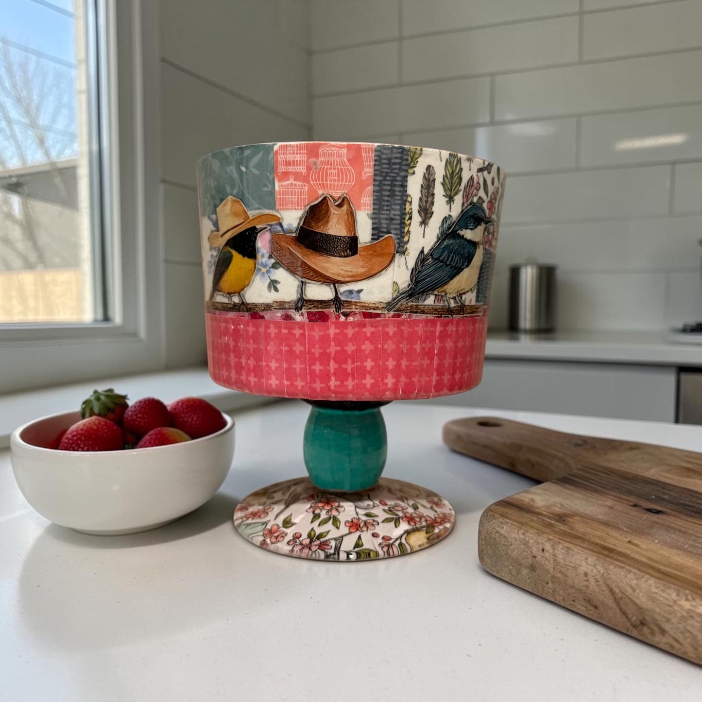Decorated trifle bowl on a kitchen counter next to a bowl of tomatoes and a cutting board.